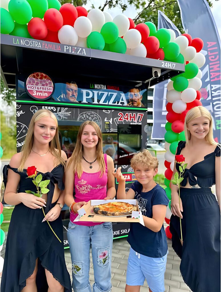Pizza vending machine launch event with customers holding fresh pizza in front of an outdoor machine