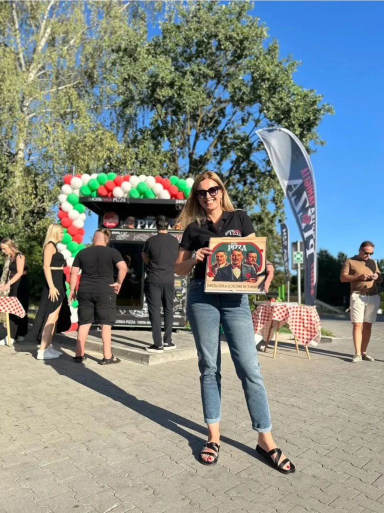 Outdoor pizza vending machine opening event with customers and a branded pizza box in front of the machine